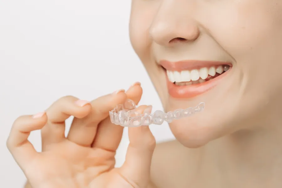 Patient holding a clear aligner near their smile